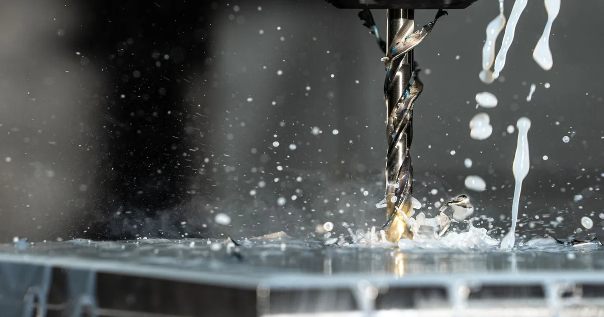 Twist drill with coolant spray cutting into a metal workpiece, the set-up used when drilling tungsten with carbide tools